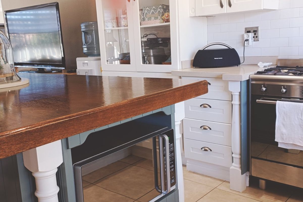 A well-appointed kitchen featuring a large wooden-topped island, stainless steel gas range, built-in microwave, and classic white shaker cabinetry with subway tile backsplash.