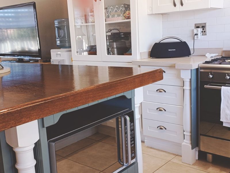 A well-appointed kitchen featuring a large wooden-topped island, stainless steel gas range, built-in microwave, and classic white shaker cabinetry with subway tile backsplash.