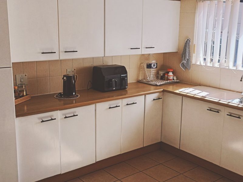 A functional kitchen featuring white cabinetry, laminate countertops, tiled backsplash, and a double basin sink with a mixer tap.