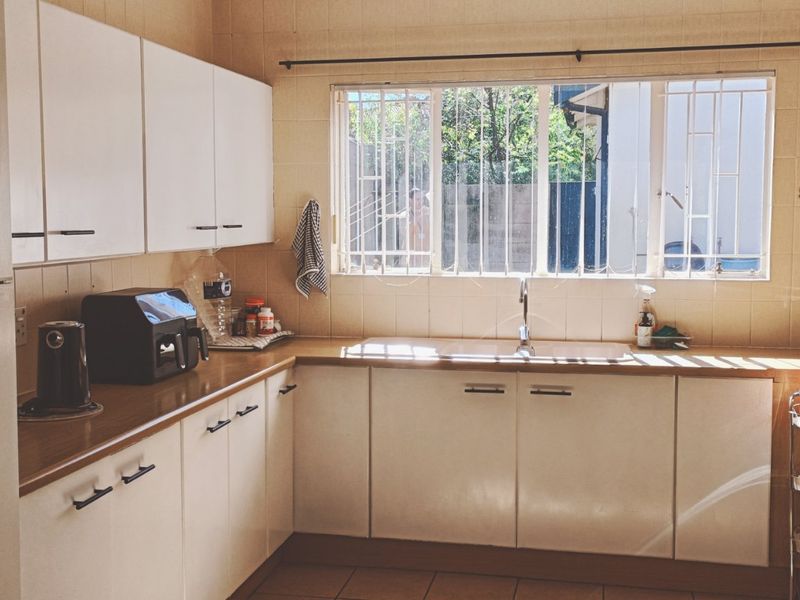 A functional kitchen featuring white cabinetry, laminate countertops, a double basin sink, and tiled splashbacks with natural light from a window with security bars.