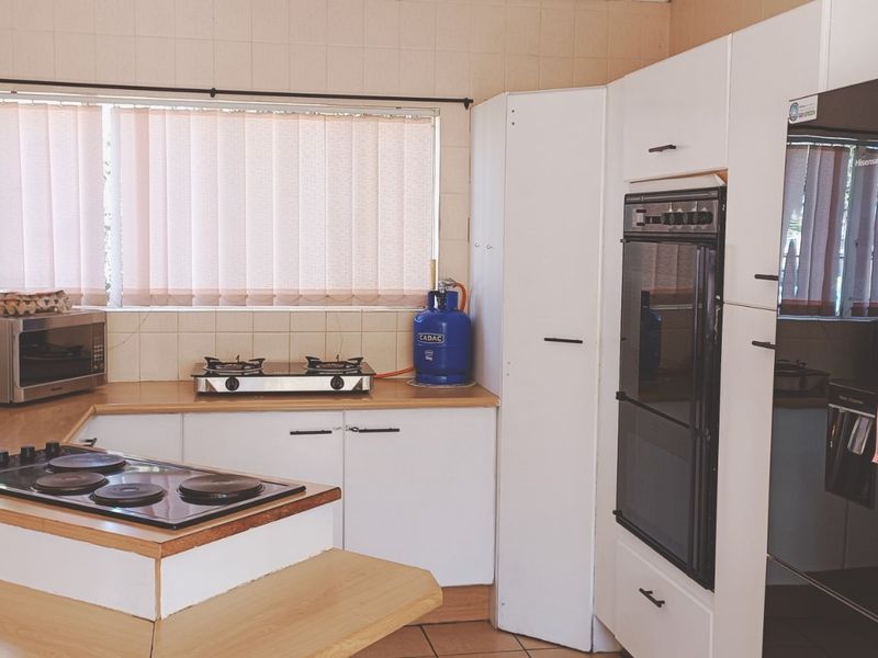 A functional kitchen featuring white cabinetry, laminate countertops, a built-in oven, and an electric hob with tiled wall finishes.