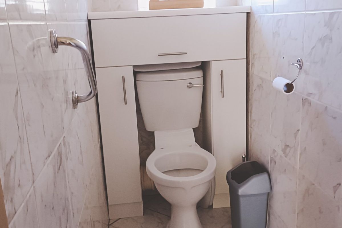 A compact bathroom featuring a white toilet with a built-in storage vanity unit, tiled walls, and a safety grab rail.