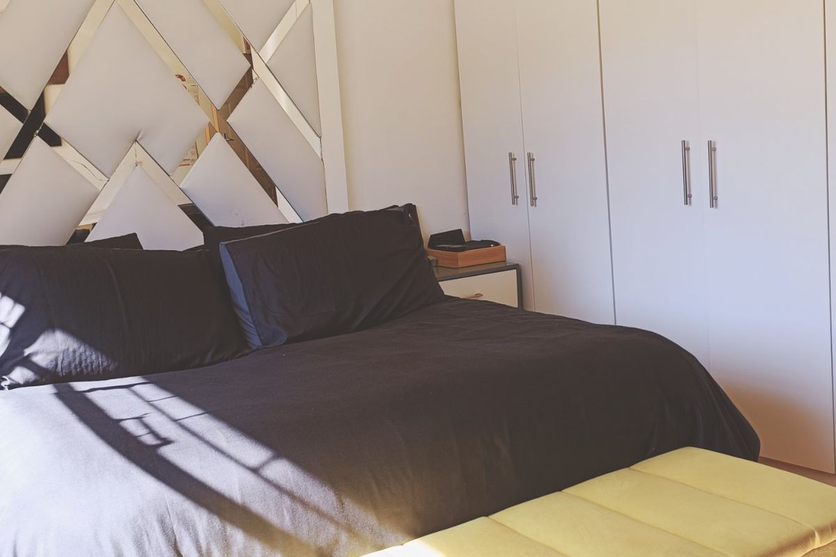 A well-maintained bedroom featuring extensive built-in cupboards and a decorative mirrored headboard wall feature.
