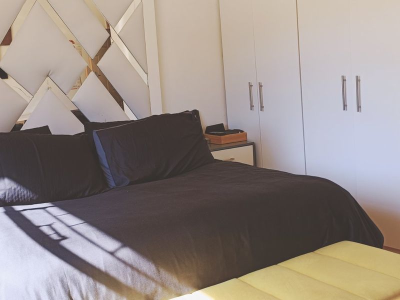 A well-maintained bedroom featuring extensive built-in cupboards and a decorative mirrored headboard wall feature.