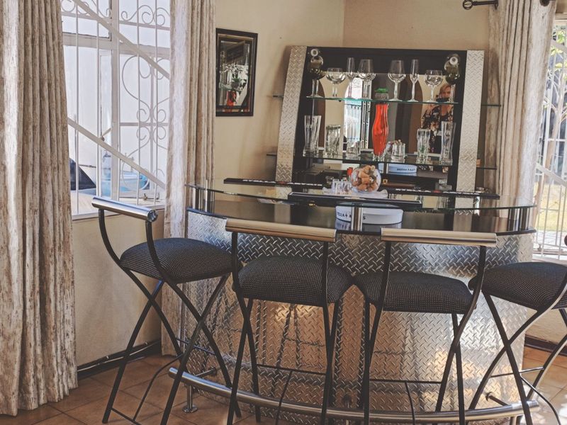 A dedicated bar area featuring a built-in counter with metal cladding, glass shelving, and tiled flooring, set within a bright room with security-barred windows.
