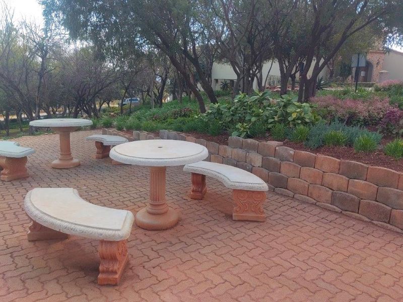 A landscaped garden area featuring a paved patio with stone seating and a retaining wall, surrounded by mature trees and shrubs.
