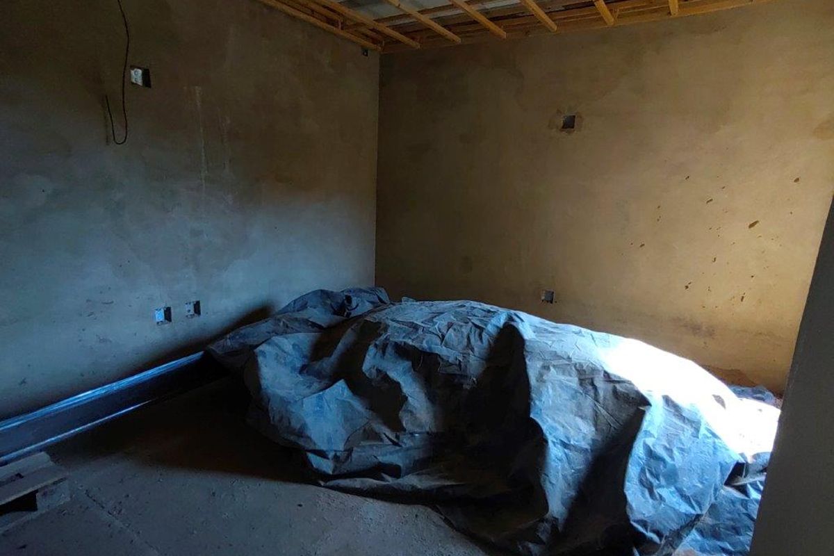 An unfinished bedroom space featuring exposed timber ceiling joists, raw plastered walls, and basic electrical infrastructure, currently in a shell condition.
