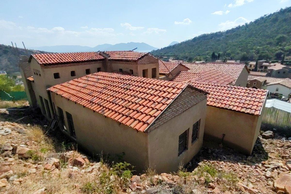 Aerial view of a residential property under construction, featuring terracotta roof tiles and unfinished exterior walls set against a hillside landscape.