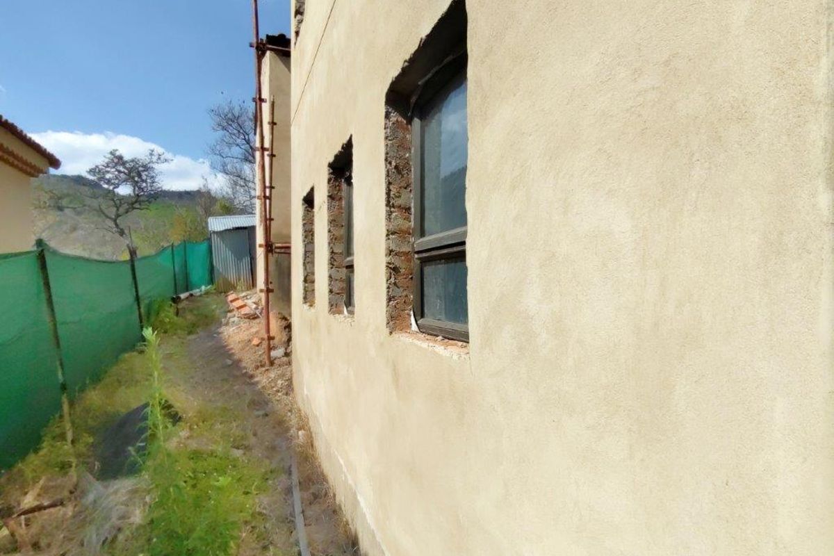 Side view of the property showing unfinished exterior plastering and exposed brickwork around the installed aluminium window frames.