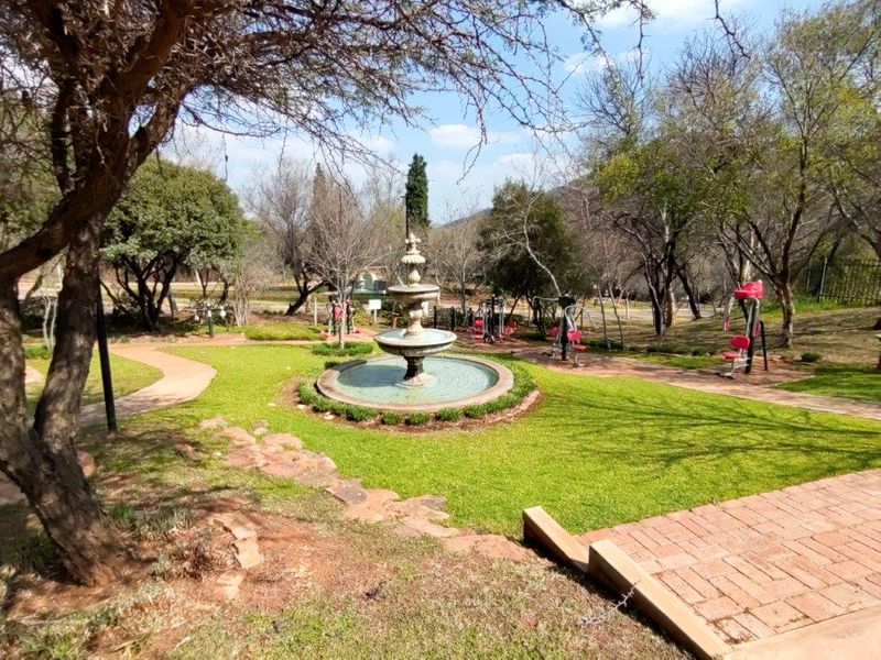 A well-maintained garden area featuring a central stone fountain, paved pathways, and integrated outdoor exercise equipment set within a landscaped green space.