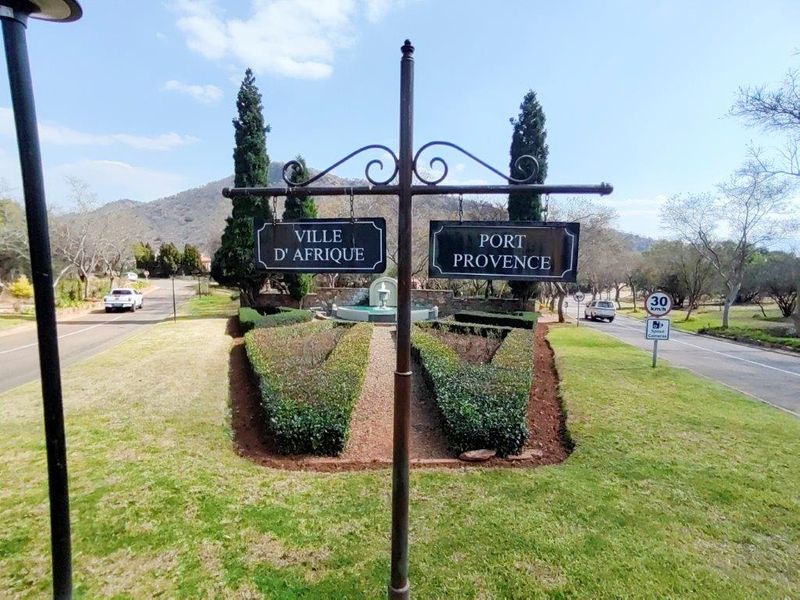 Entrance view of the estate featuring manicured gardens, a central water fountain, and signage for Ville D'Afrique and Port Provence.