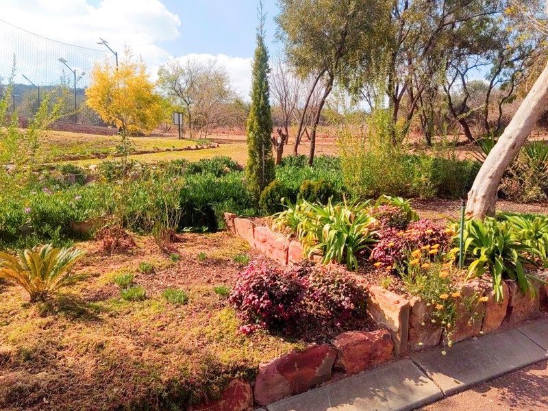 A landscaped garden area featuring stone retaining walls, established shrubs, and mature trees in a natural outdoor setting.