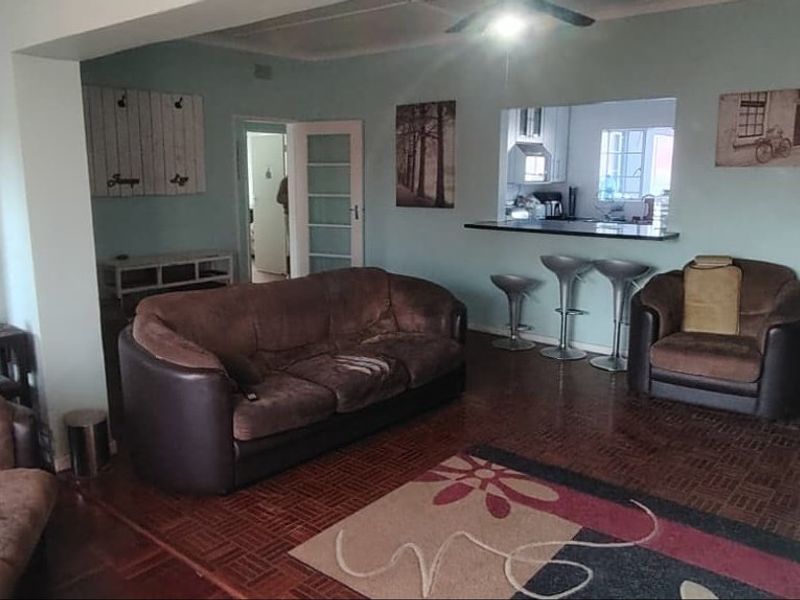 Open plan living area featuring parquet flooring, a breakfast bar with a pass-through window to the kitchen, and a ceiling fan.