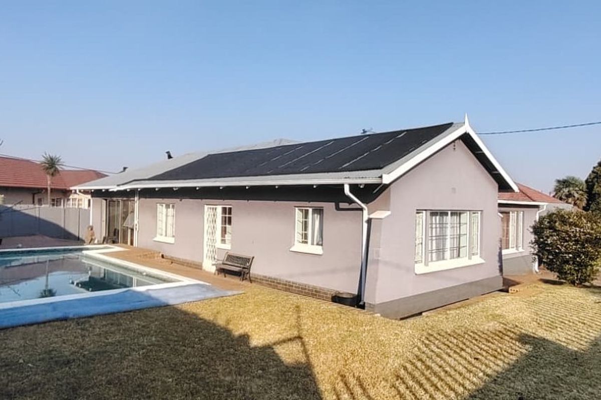 Rear view of the property featuring a swimming pool, solar panel installation on the roof, and a well-maintained garden area.