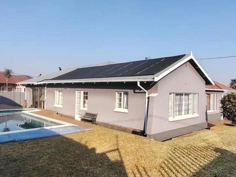Rear view of the property featuring a swimming pool, solar panel installation on the roof, and a well-maintained garden area.