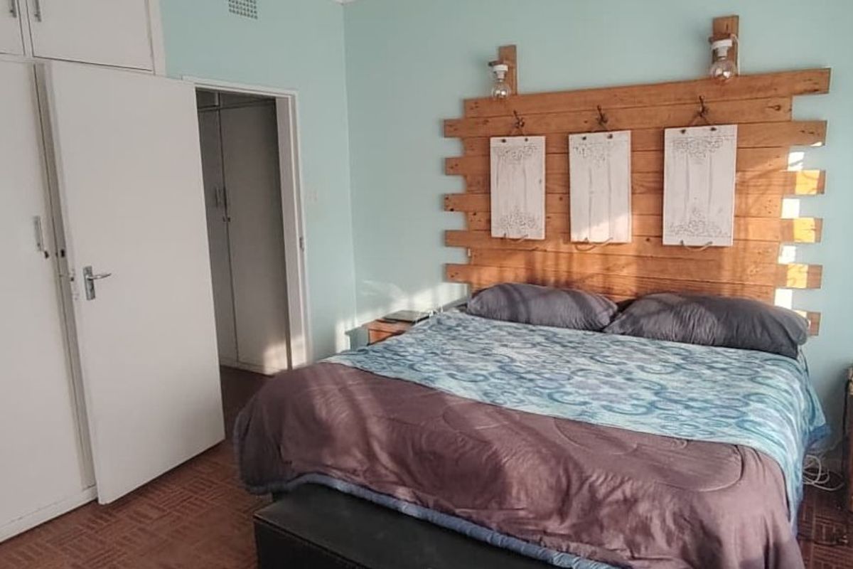 A bedroom featuring built-in cupboards, parquet flooring, and a ceiling vent, offering a functional space with potential for modern updates.