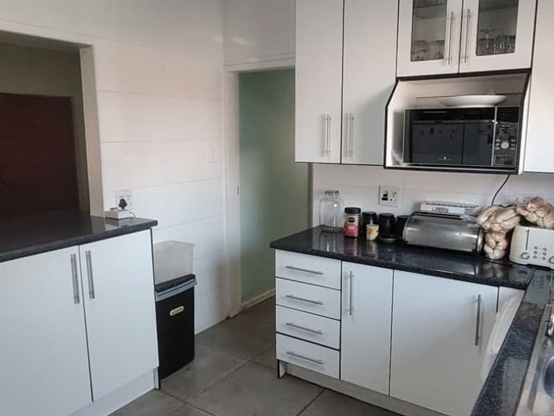 A functional kitchen featuring white cabinetry, dark laminate countertops, and a stainless steel sink, with an open-plan layout connecting to the adjacent living area.