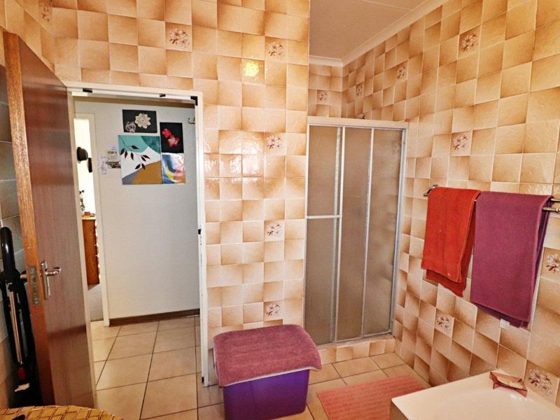 A functional bathroom featuring a shower enclosure and dated wall tiling throughout, offering potential for a modern renovation.