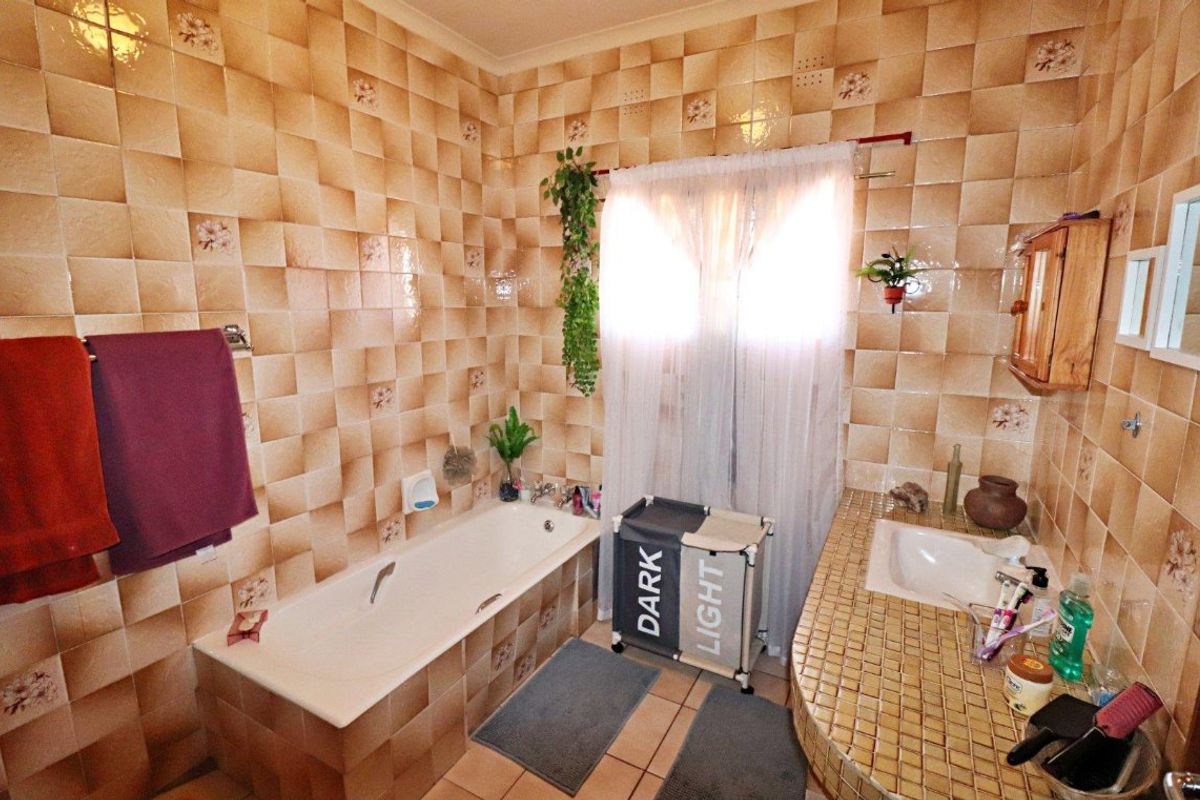 A dated bathroom featuring a built-in bathtub and a tiled vanity countertop with an integrated sink, finished with patterned ceramic wall tiles.