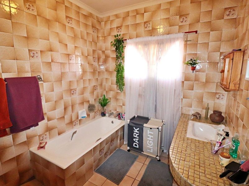 A dated bathroom featuring a built-in bathtub and a tiled vanity countertop with an integrated sink, finished with patterned ceramic wall tiles.