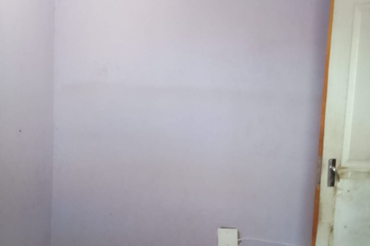 An empty bedroom featuring tiled flooring and light purple walls, requiring minor cosmetic updates to the paint and door finish.