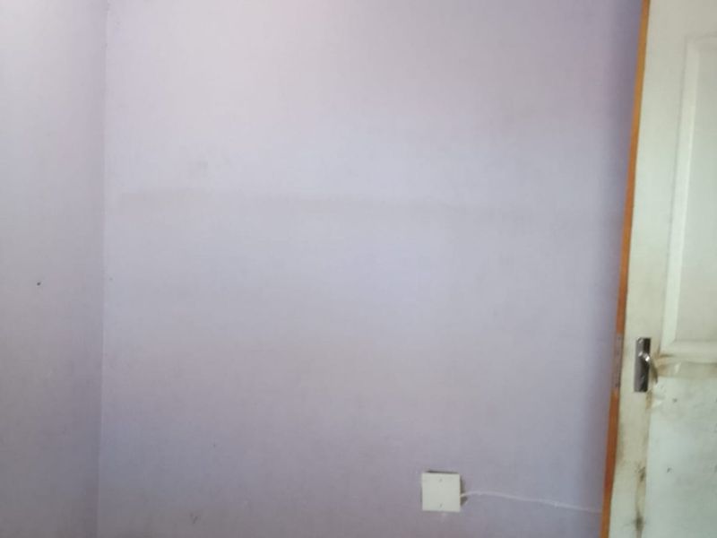 An empty bedroom featuring tiled flooring and light purple walls, requiring minor cosmetic updates to the paint and door finish.