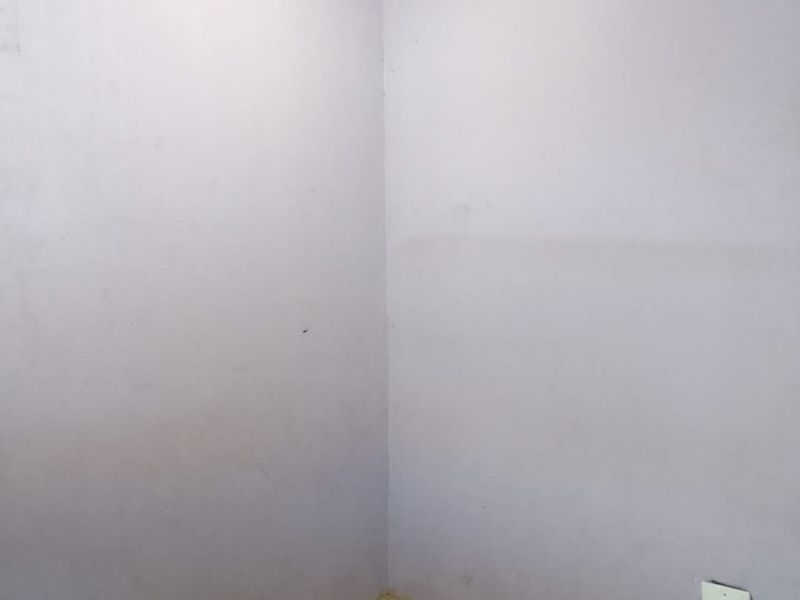 A vacant corner of a room featuring tiled flooring, coving, and light purple painted walls with visible scuff marks.
