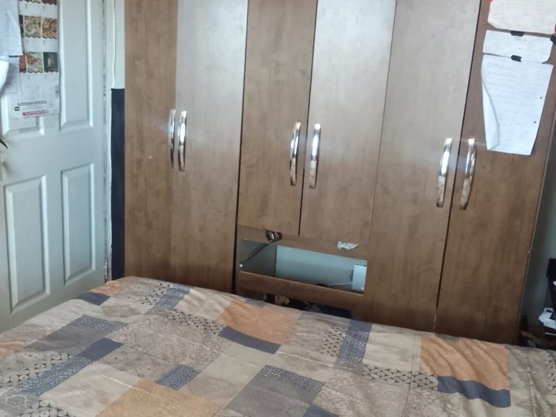 A bedroom featuring a built-in wooden wardrobe with a visible damaged section on one of the lower cabinet doors.