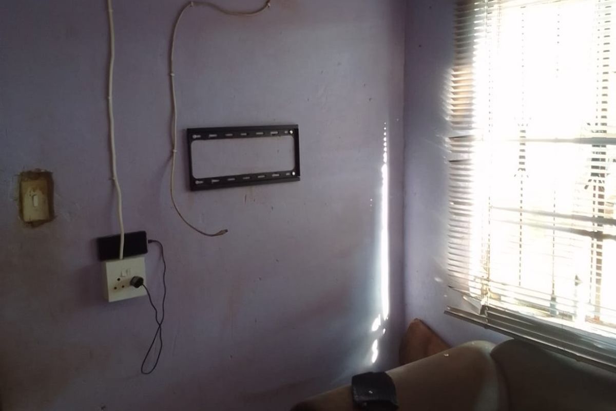 A living room area featuring a wall-mounted TV bracket, venetian blinds, and visible electrical wiring requiring maintenance and cosmetic updates.