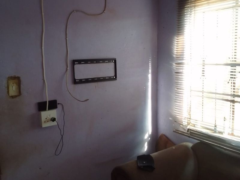A living room area featuring a wall-mounted TV bracket, venetian blinds, and visible electrical wiring requiring maintenance and cosmetic updates.