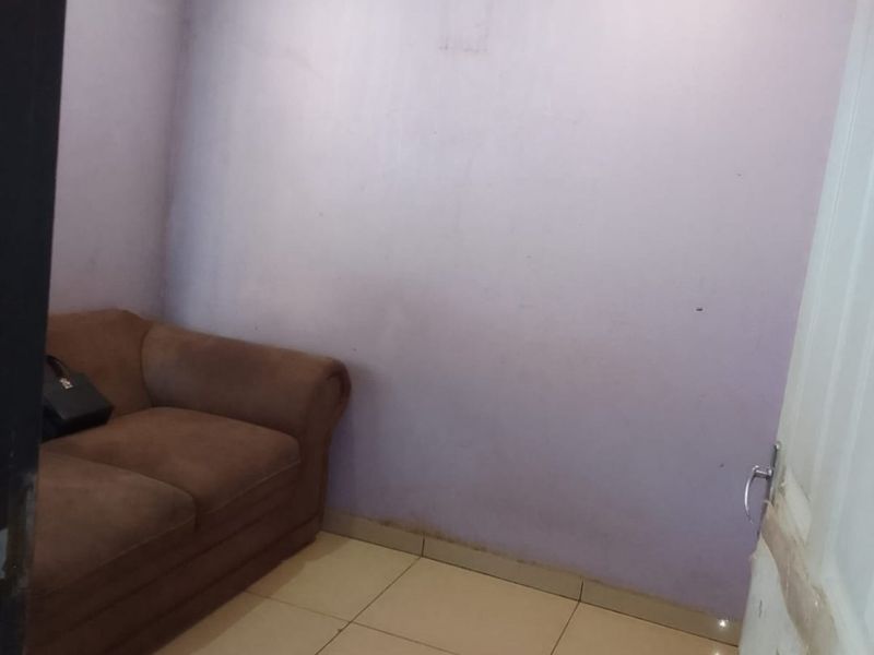 A small bedroom featuring tiled flooring and recessed ceiling lighting, currently requiring cosmetic updates to the wall finishes and door frame.