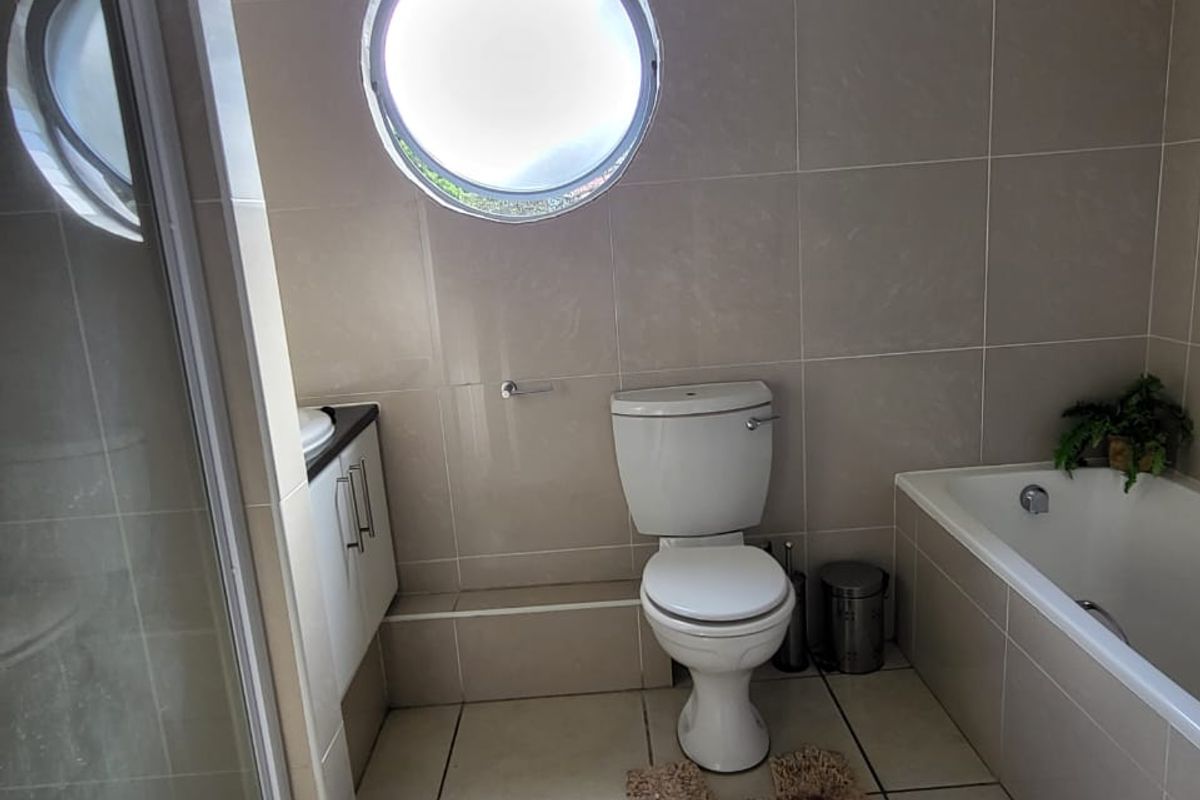 A functional bathroom featuring a built-in bathtub, separate shower enclosure, vanity unit, and a distinctive circular window with neutral wall and floor tiling.
