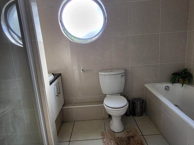 A functional bathroom featuring a built-in bathtub, separate shower enclosure, vanity unit, and a distinctive circular window with neutral wall and floor tiling.