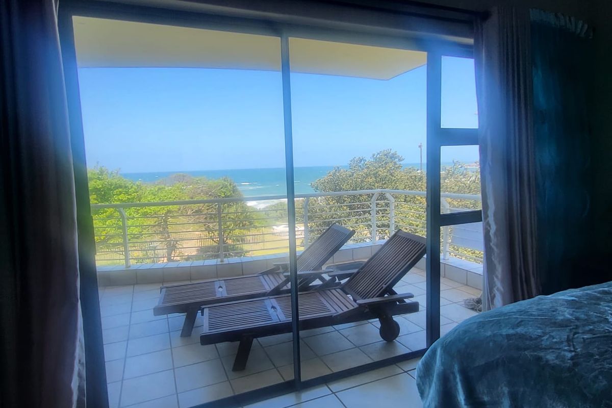 A balcony featuring tiled flooring and a metal balustrade, offering scenic ocean views accessible through a large sliding glass door.