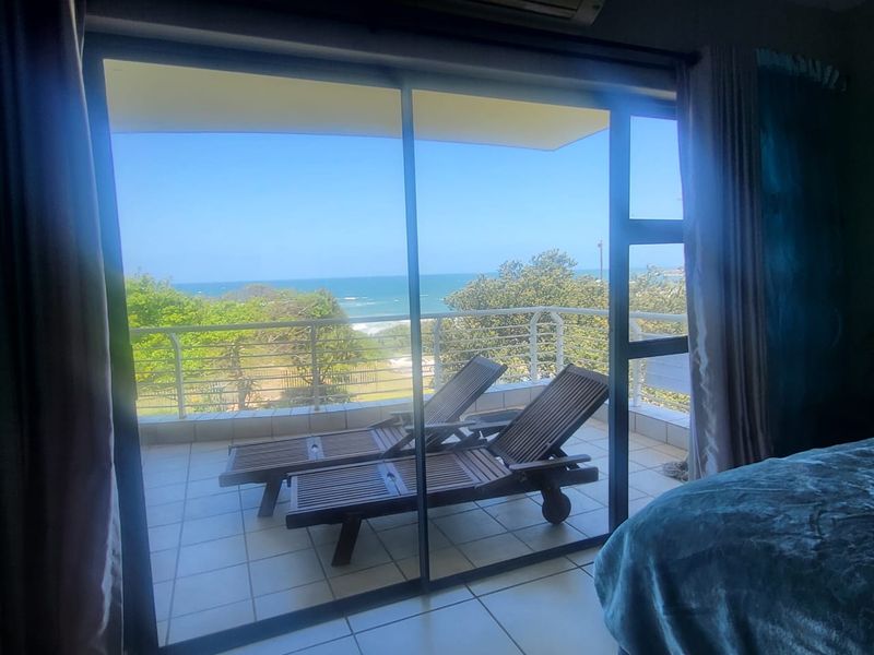 A balcony featuring tiled flooring and a metal balustrade, offering scenic ocean views accessible through a large sliding glass door.