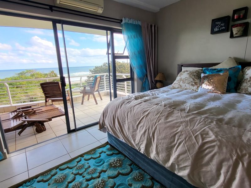 Spacious bedroom featuring tiled floors, a wall-mounted air conditioner, and large sliding glass doors opening onto a private balcony with ocean views.