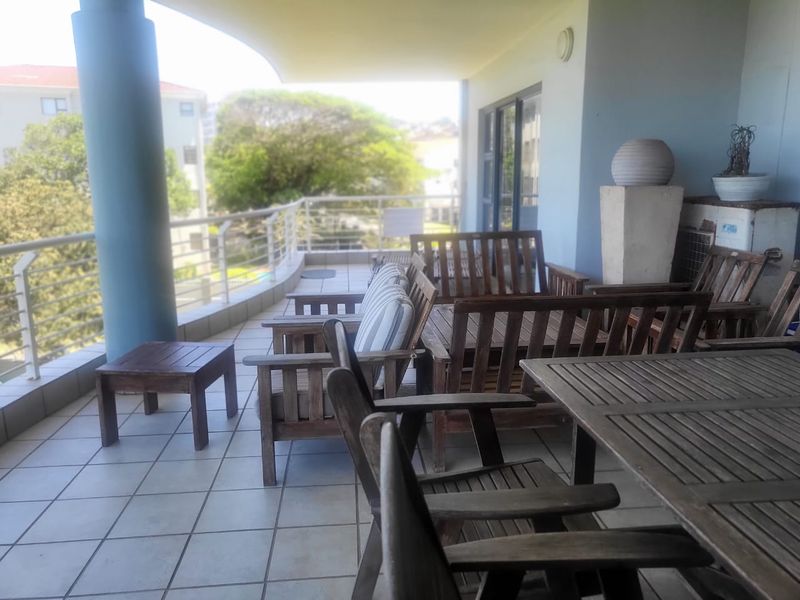 A spacious covered balcony featuring tiled flooring, a metal balustrade, and a structural column, offering an open-air outdoor living space.