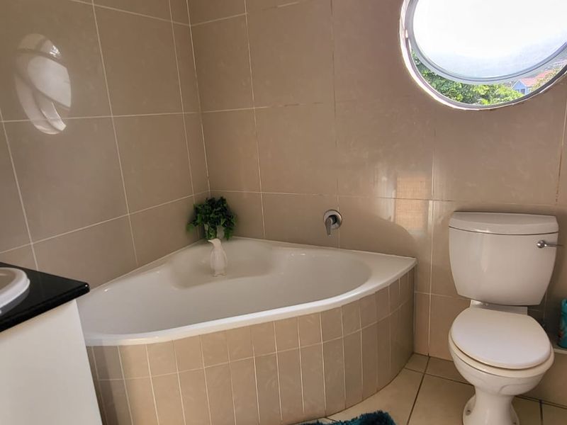 A functional bathroom featuring a corner bathtub, ceramic wall and floor tiles, and a distinctive circular porthole window.