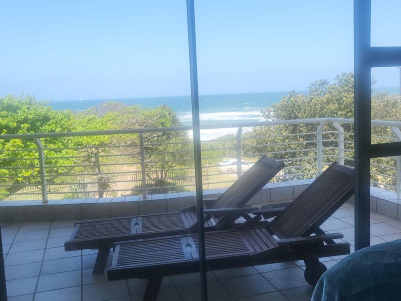 A tiled balcony featuring a metal balustrade and direct ocean views, accessible via a large sliding glass door.
