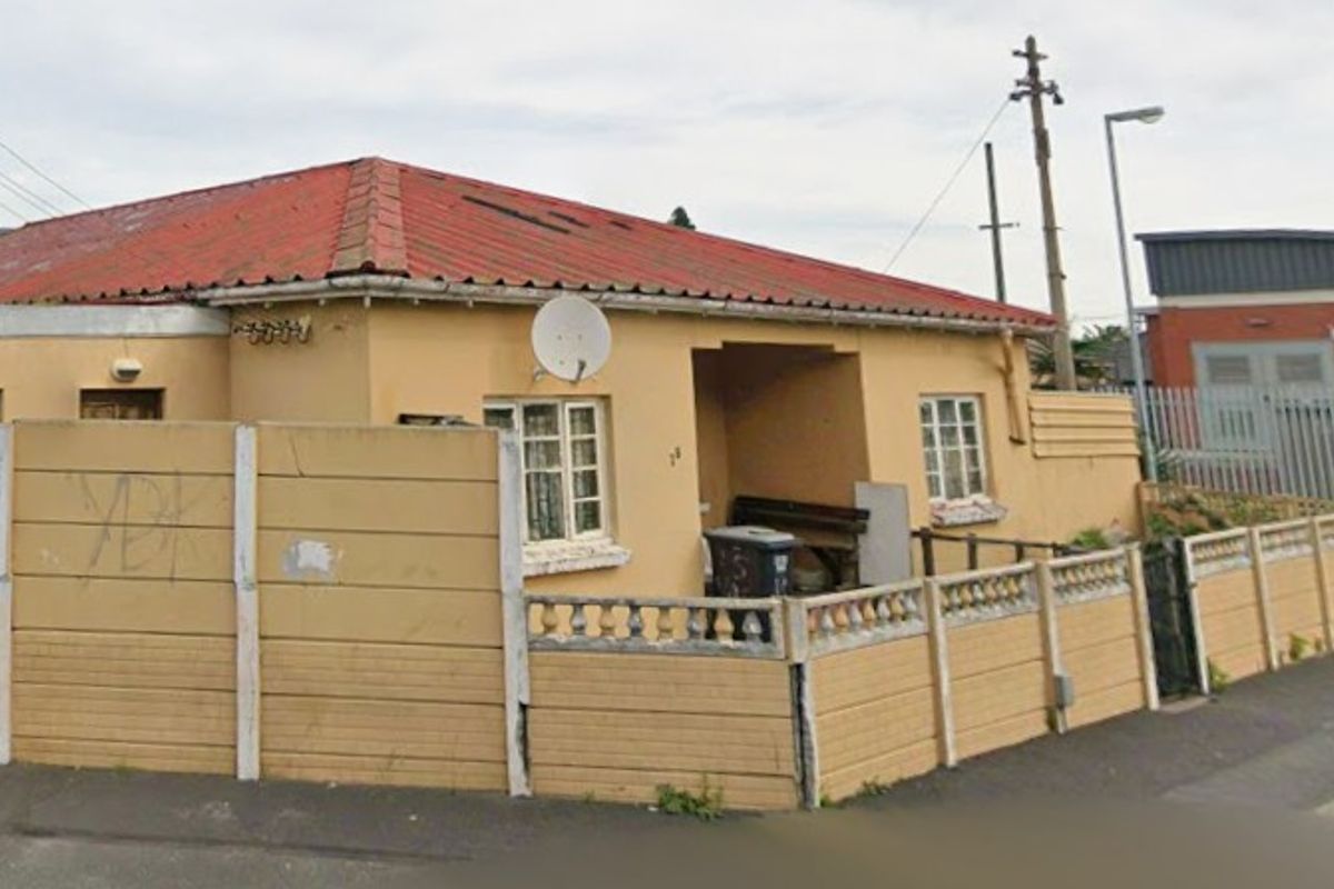 Street-facing view of a single-story house featuring a tiled roof and a precast concrete boundary wall with visible signs of wear.