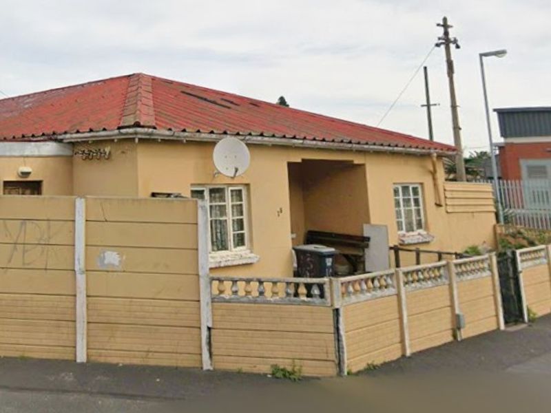 Street-facing view of a single-story house featuring a tiled roof and a precast concrete boundary wall with visible signs of wear.