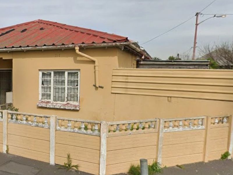 Front elevation of a single-story house featuring a corrugated metal roof, security-barred windows, and a precast concrete boundary wall.