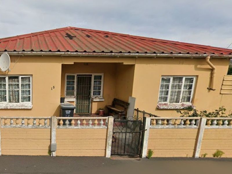 Front elevation of a single-story house featuring a corrugated metal roof, precast concrete boundary wall, and security features on windows and entrance.