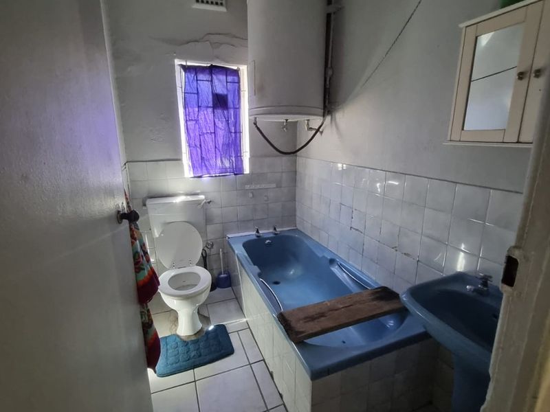 A dated bathroom featuring a blue bathtub and pedestal basin, tiled flooring, and an exposed electric water heater.