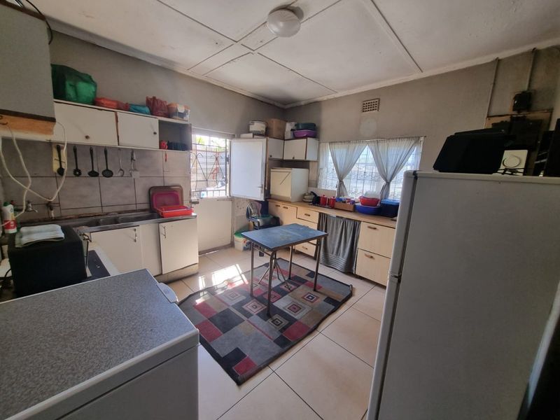 A functional kitchen featuring built-in cabinetry, tiled splashbacks, and tiled flooring, offering a practical layout with potential for modern updates.