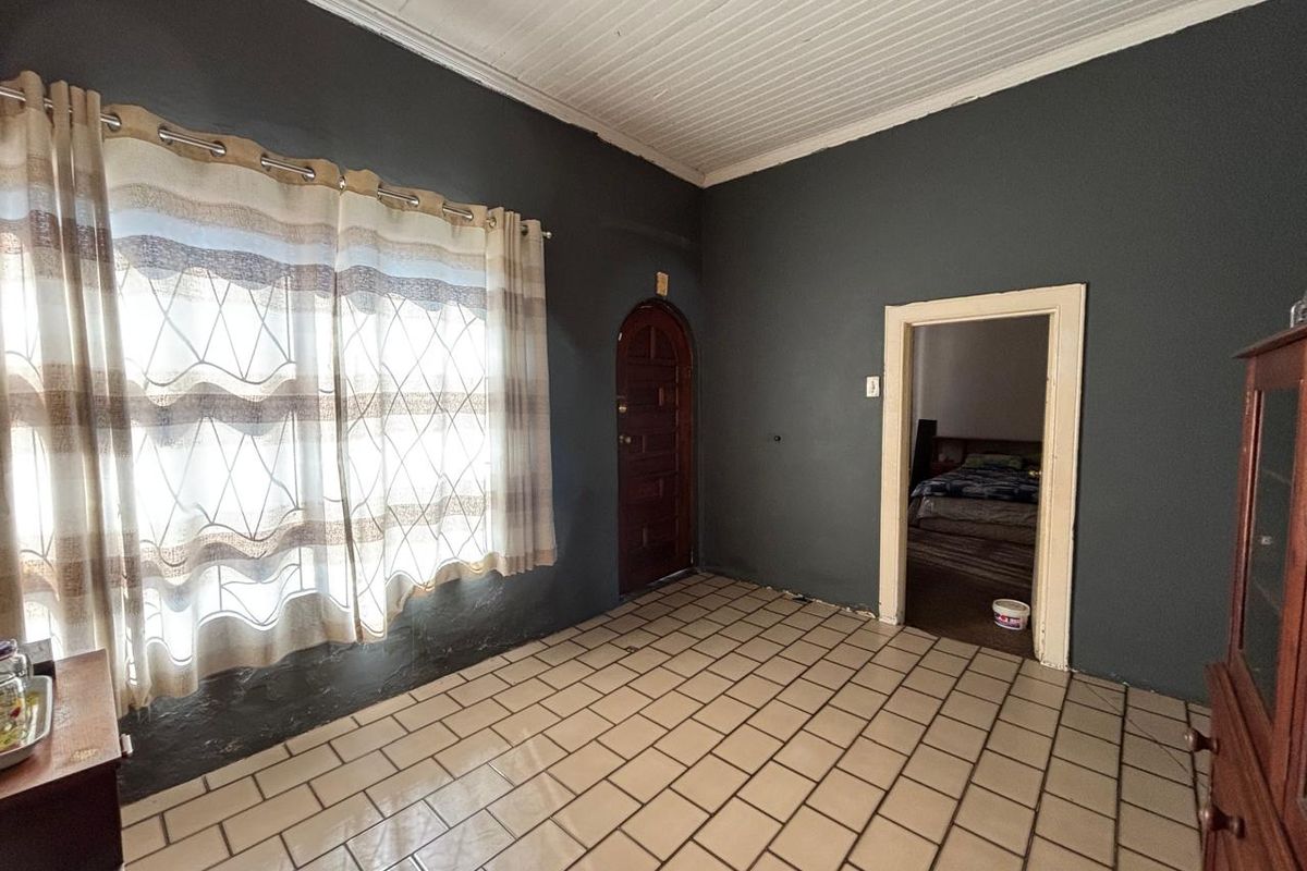 A living area featuring tiled flooring, a distinctive arched wooden door, and a tongue and groove ceiling, requiring some cosmetic attention to the walls.