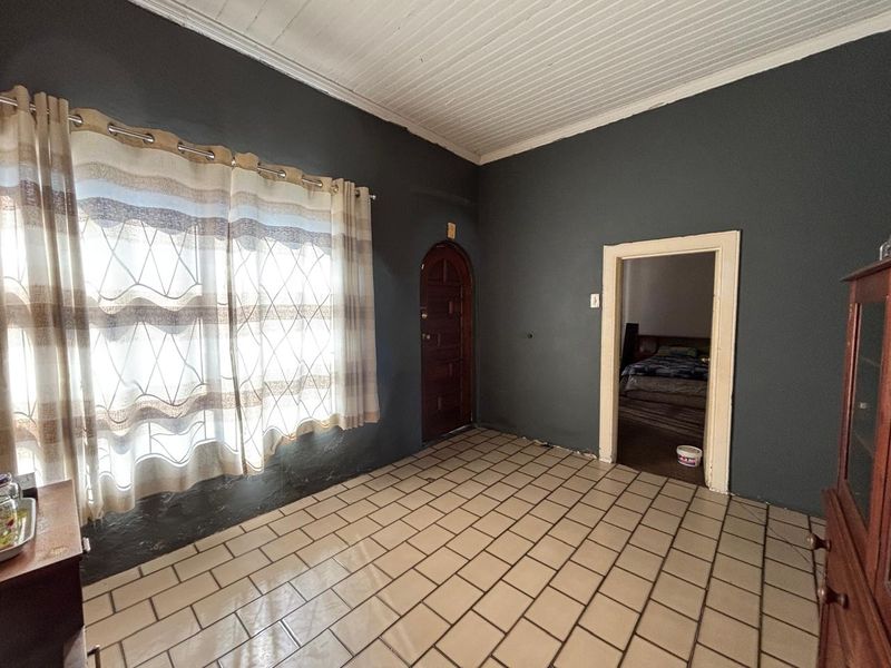 A living area featuring tiled flooring, a distinctive arched wooden door, and a tongue and groove ceiling, requiring some cosmetic attention to the walls.