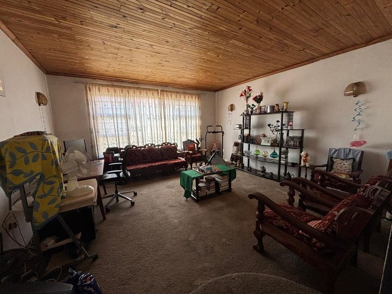 A spacious living room featuring a warm timber tongue and groove ceiling and wall-to-wall carpeting, offering a comfortable and traditional living space.