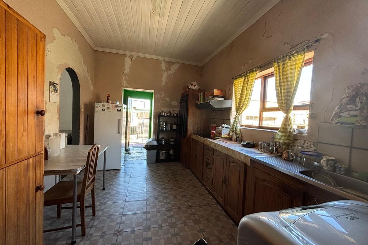 A dated kitchen featuring wooden cabinetry, a tiled countertop, and a timber ceiling, currently requiring significant cosmetic renovation and wall repairs.