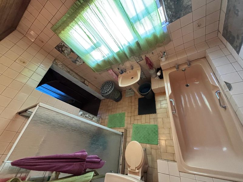 A dated bathroom featuring a peach-colored bathtub, pedestal basin, and shower enclosure with extensive wall tiling in need of repair and modernization.
